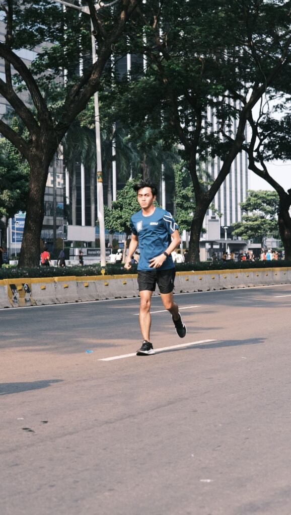About A young man running outdoors on an urban street surrounded by trees during the day.