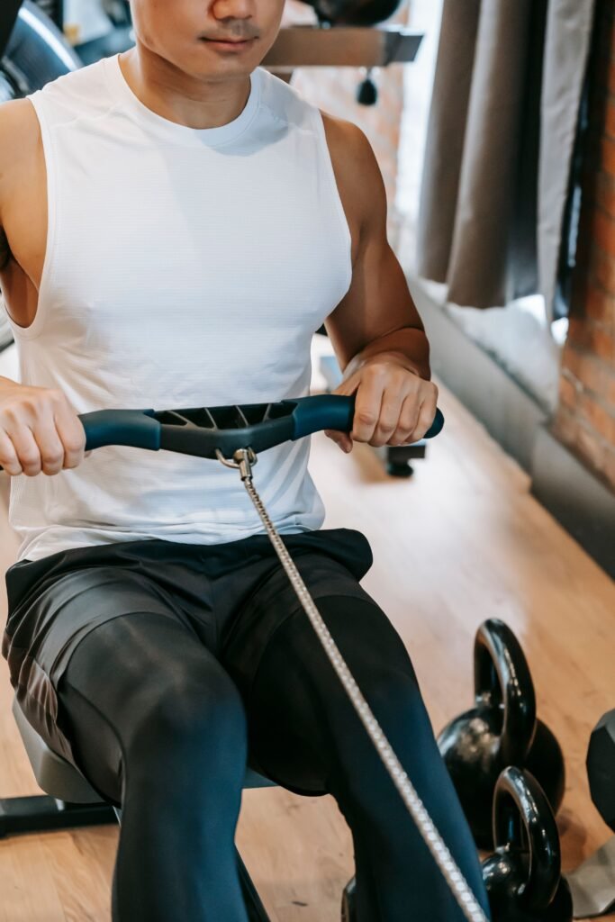 About High angle of crop focused strong male athlete in sportswear doing exercise on rowing machine during training